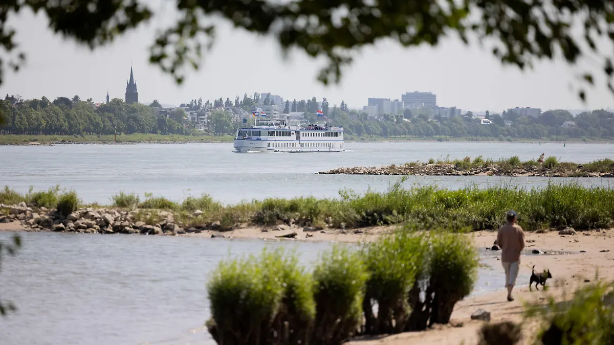 30.05.2023, Nordrhein-Westfalen, Köln: Eine Mann und sein Hund gehen bei Sonnenschein im Sand am Rhein in Rodenkirchen spazieren. Laut dem Deutschen Wetterdienst, soll das Wetter in den nächsten Tagen sonnig bei Temperaturen über 20°C bleiben. Foto: Rolf Vennenbernd/dpa +++ dpa-Bildfunk +++