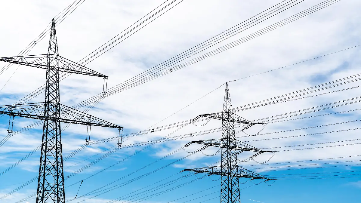 Mehrere Strommasten mit Hochspannungsleitungen vor blauem Himmel zeigen die Verteilung elektrischer Energie. Das Bild steht für Stromversorgung, steigende Energiepreise und die Bedeutung stabiler Netze in der Energiepolitik.