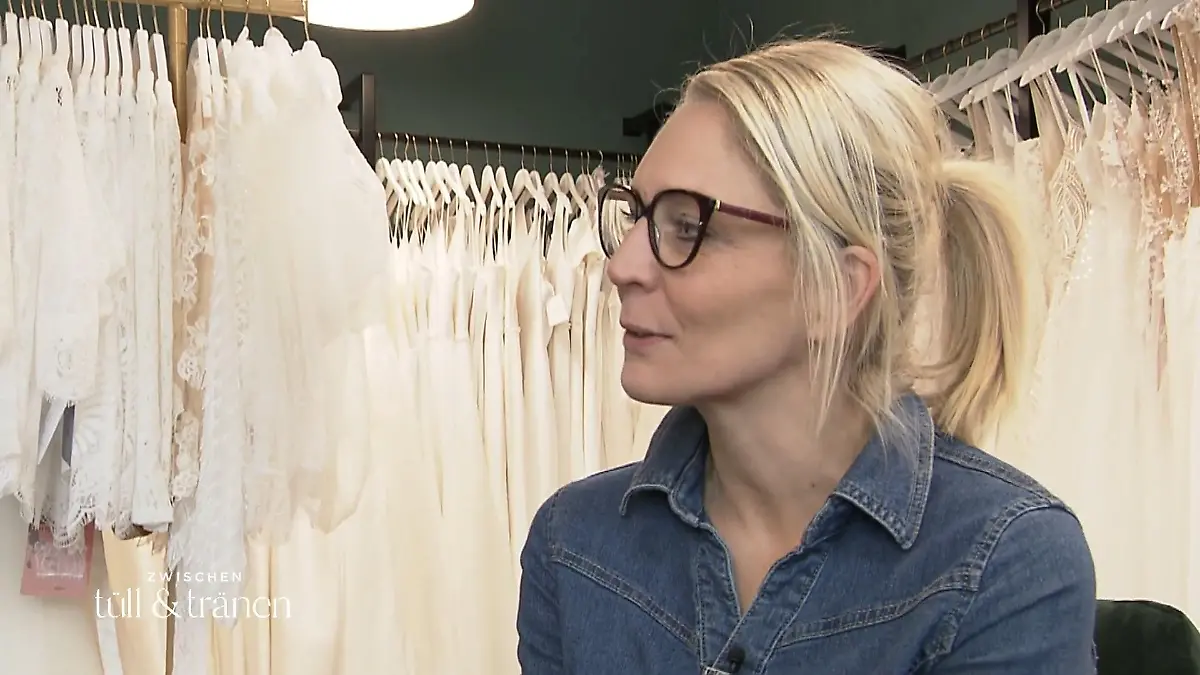 Nadine sitzt vor Kleiderständern mit Brautkleidern.