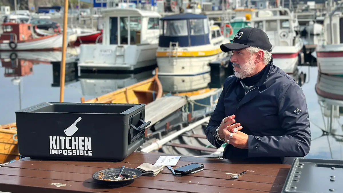 Roland Trettl sitz an einem Tisch im Hafen, darauf ein leer gegessener Teller, eine große Box und Notizen.