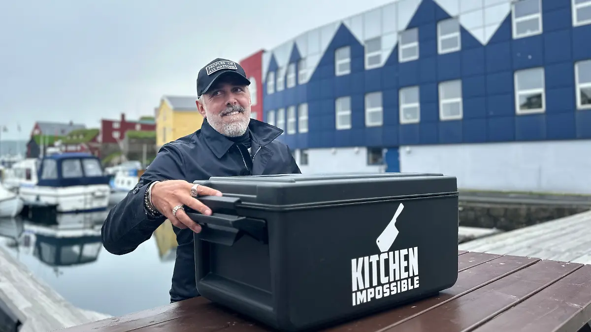 Roland Trettl an einem Tisch im Hafen. vor ihm eine große schwarze Box, er schaut skeptisch. 