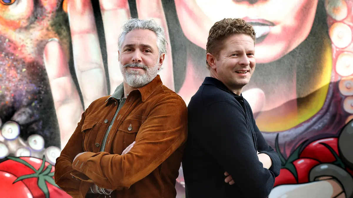 Die beiden Köche stehen Rücken an Rücken, die Arme verschränkt, leichtes Lächeln