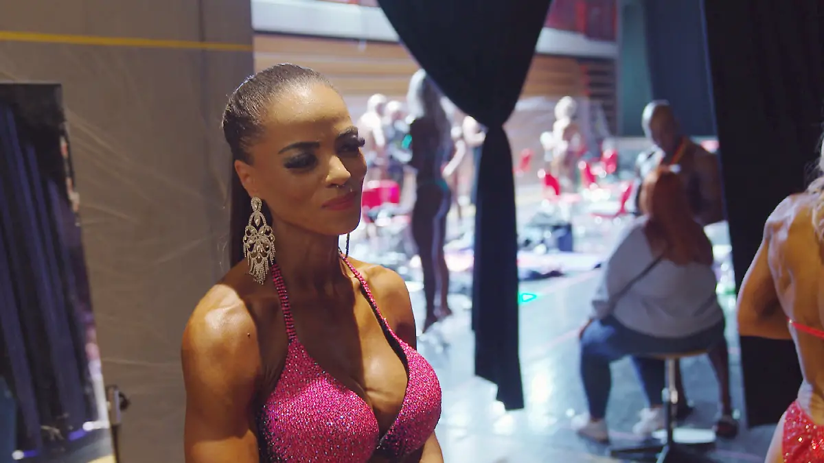 Für immer jung: Schlanke, muskulöse Frau im pinkfarbenen Glitzerbikini vor einem Bodybuilding-Auftritt