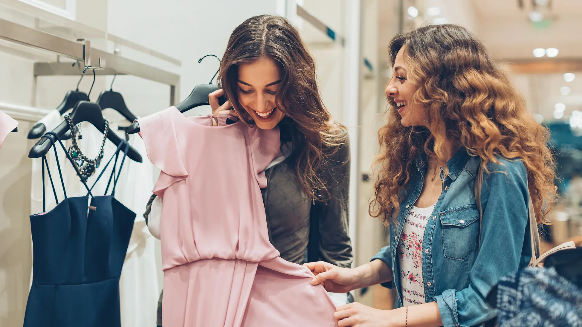 Zwei Frauen sind in einem Kleidungsgeschäft und suchen Kleider aus.