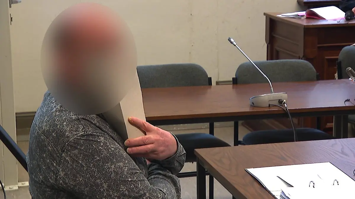 Der Angeklagte sitzt in einem Gericht und verdeckt sein Gesicht mit Papier.