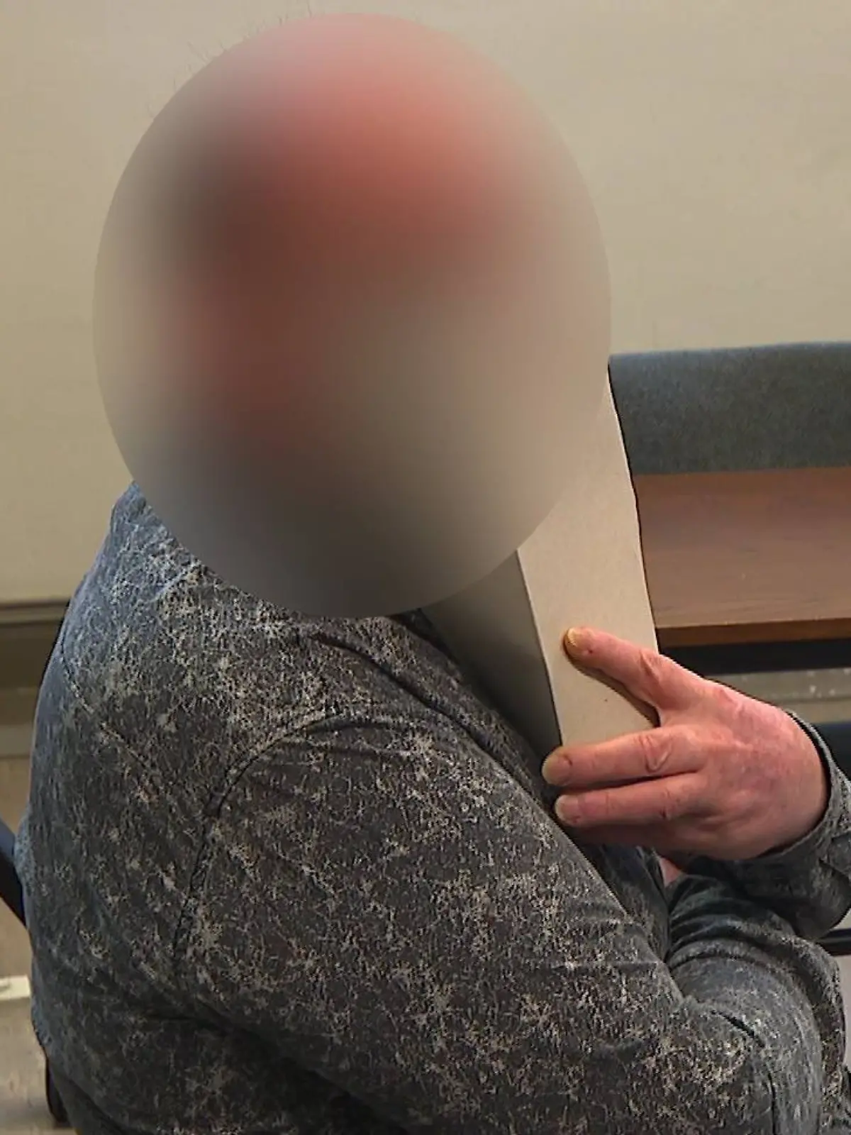 Der Angeklagte sitzt in einem Gericht und verdeckt sein Gesicht mit Papier.