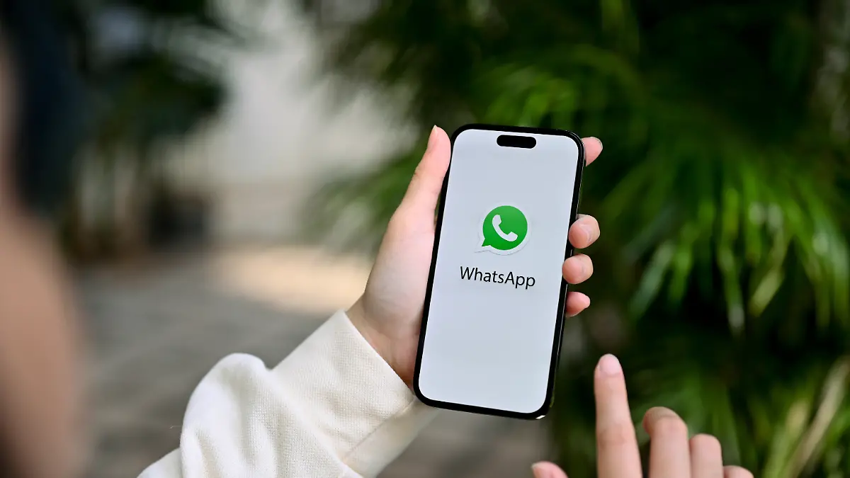Nahaufnahme einer Frau, die mit ihren Freunden über die WhatsApp-App chattet; sie hält ein iPhone mit dem WhatsApp-Logo auf dem Bildschirm in der Hand.