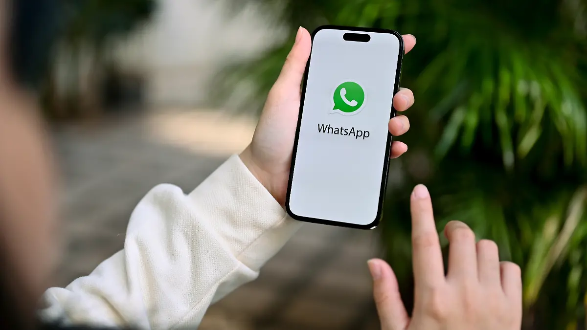 Nahaufnahme einer Frau, die mit ihren Freunden über die WhatsApp-App chattet; sie hält ein iPhone mit dem WhatsApp-Logo auf dem Bildschirm in der Hand.