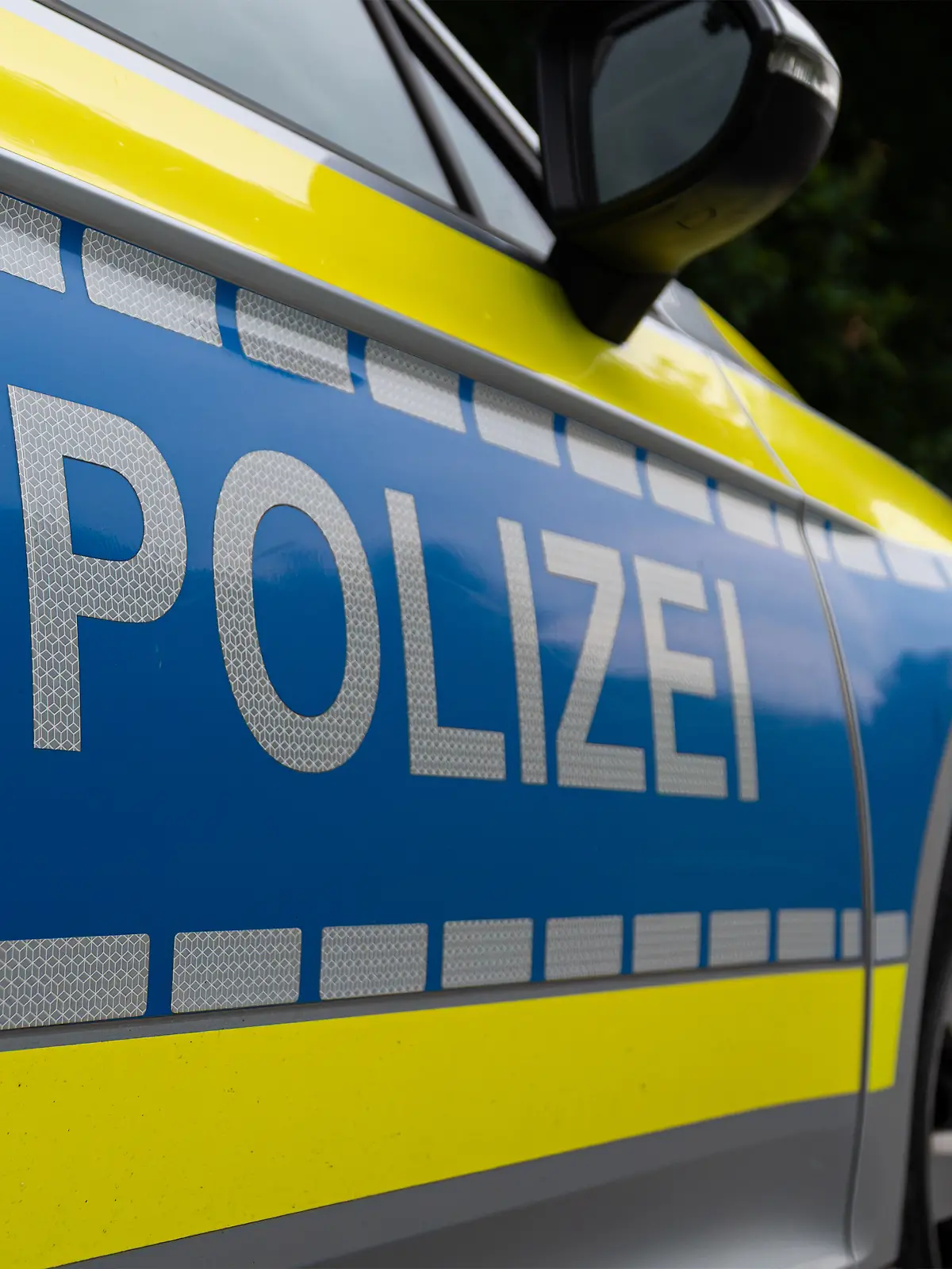 Landkreis Osnabrück, Deutschland 10. Juni 2025: Im Bild: Caption: Nahaufnahme des Seitenbereichs eines deutschen Polizeifahrzeugs mit dem markanten silberfarbenen "POLIZEI"-Schriftzug auf blauem Grund. Der Schriftzug ist auf einer reflektierenden Folie angebracht, die für erhöhte Sichtbarkeit sorgt. Auffällig ist die leuchtend gelbe Kontrastfarbe, die sich von der Motorhaube bis zur Tür zieht und von einer Reihe reflektierender Quadrate begleitet wird. Details wie der Türgriff und der Außenspiegel sind im oberen Bereich des Bildes erkennbar. Das Bild repräsentiert die Präsenz und den modernen Auftritt der deutschen Polizei.