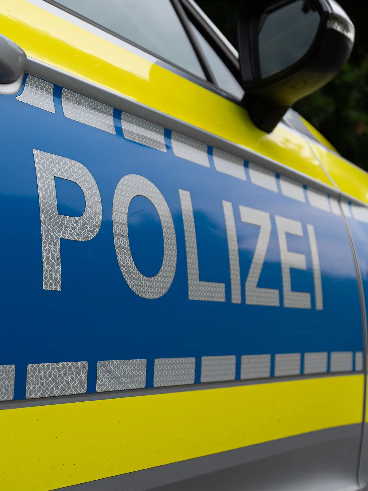 Landkreis Osnabrück, Deutschland 10. Juni 2025: Im Bild: Caption: Nahaufnahme des Seitenbereichs eines deutschen Polizeifahrzeugs mit dem markanten silberfarbenen "POLIZEI"-Schriftzug auf blauem Grund. Der Schriftzug ist auf einer reflektierenden Folie angebracht, die für erhöhte Sichtbarkeit sorgt. Auffällig ist die leuchtend gelbe Kontrastfarbe, die sich von der Motorhaube bis zur Tür zieht und von einer Reihe reflektierender Quadrate begleitet wird. Details wie der Türgriff und der Außenspiegel sind im oberen Bereich des Bildes erkennbar. Das Bild repräsentiert die Präsenz und den modernen Auftritt der deutschen Polizei.