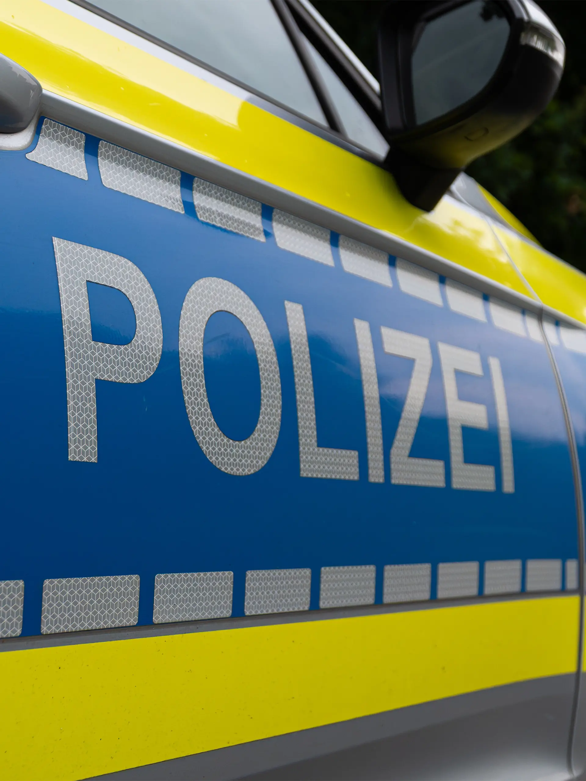 Landkreis Osnabrück, Deutschland 10. Juni 2025: Im Bild: Caption: Nahaufnahme des Seitenbereichs eines deutschen Polizeifahrzeugs mit dem markanten silberfarbenen "POLIZEI"-Schriftzug auf blauem Grund. Der Schriftzug ist auf einer reflektierenden Folie angebracht, die für erhöhte Sichtbarkeit sorgt. Auffällig ist die leuchtend gelbe Kontrastfarbe, die sich von der Motorhaube bis zur Tür zieht und von einer Reihe reflektierender Quadrate begleitet wird. Details wie der Türgriff und der Außenspiegel sind im oberen Bereich des Bildes erkennbar. Das Bild repräsentiert die Präsenz und den modernen Auftritt der deutschen Polizei.