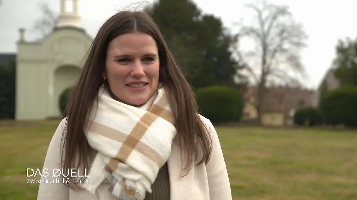 Das Duell - Zwischen Tüll und Tränen: Junge Frau mit langen braunen Haaren heller Jacke und beigefarbenem Karo-Muster-Schal steht in einem Schlosspark