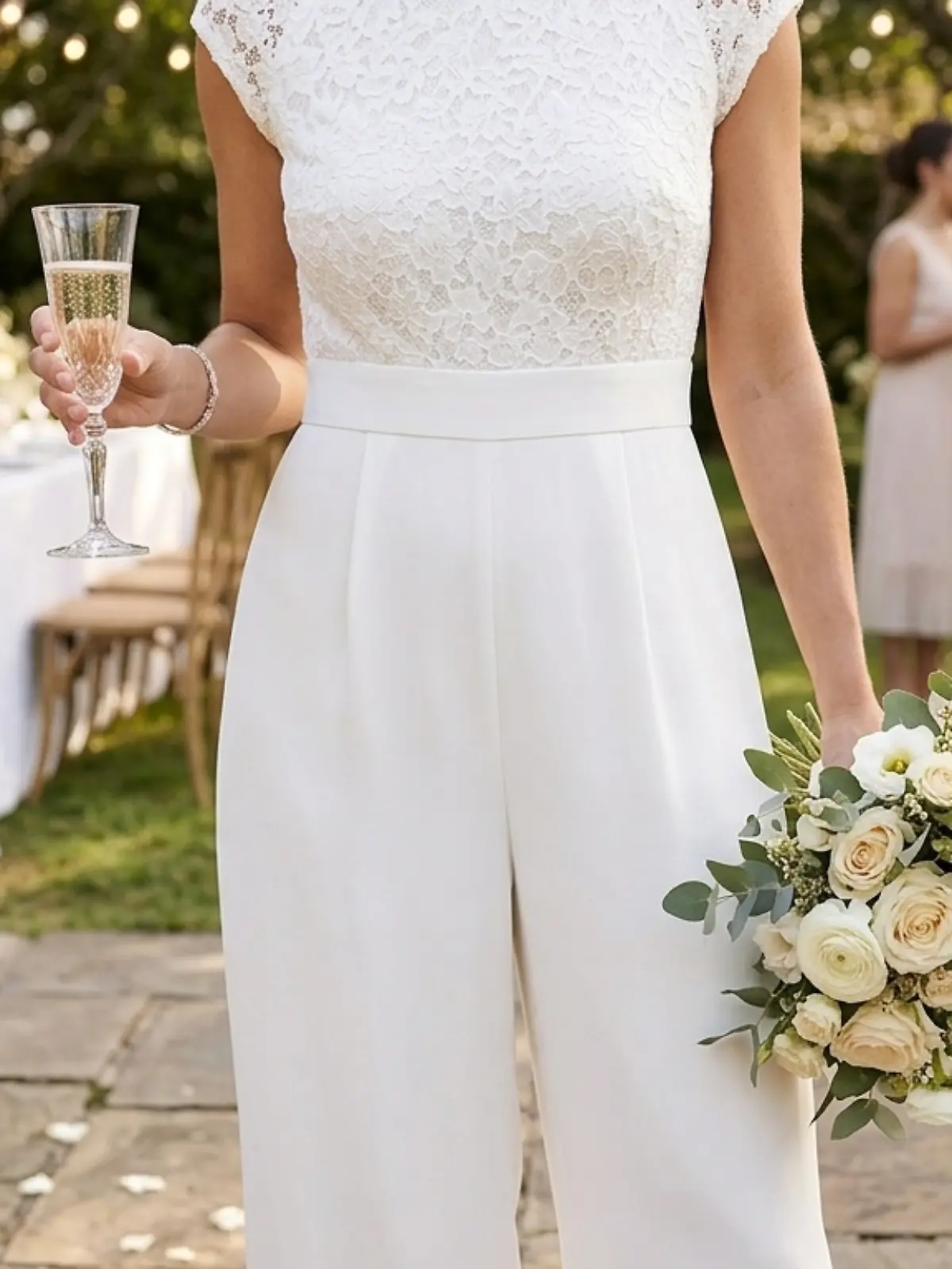 Eine Braut trägt einen Jumpsuit zur Hochzeit und hält einen Blumenstrauß und ein Glas Sekt. 