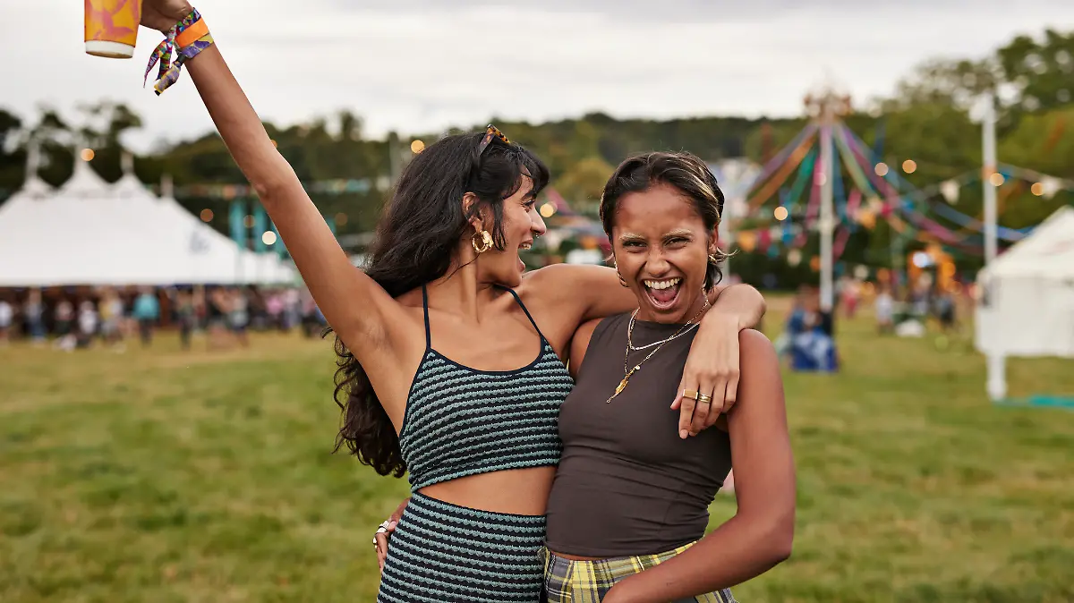 Zwei Frauen sind auf einem Festival und jubeln mit einem Getränk in der Hand.