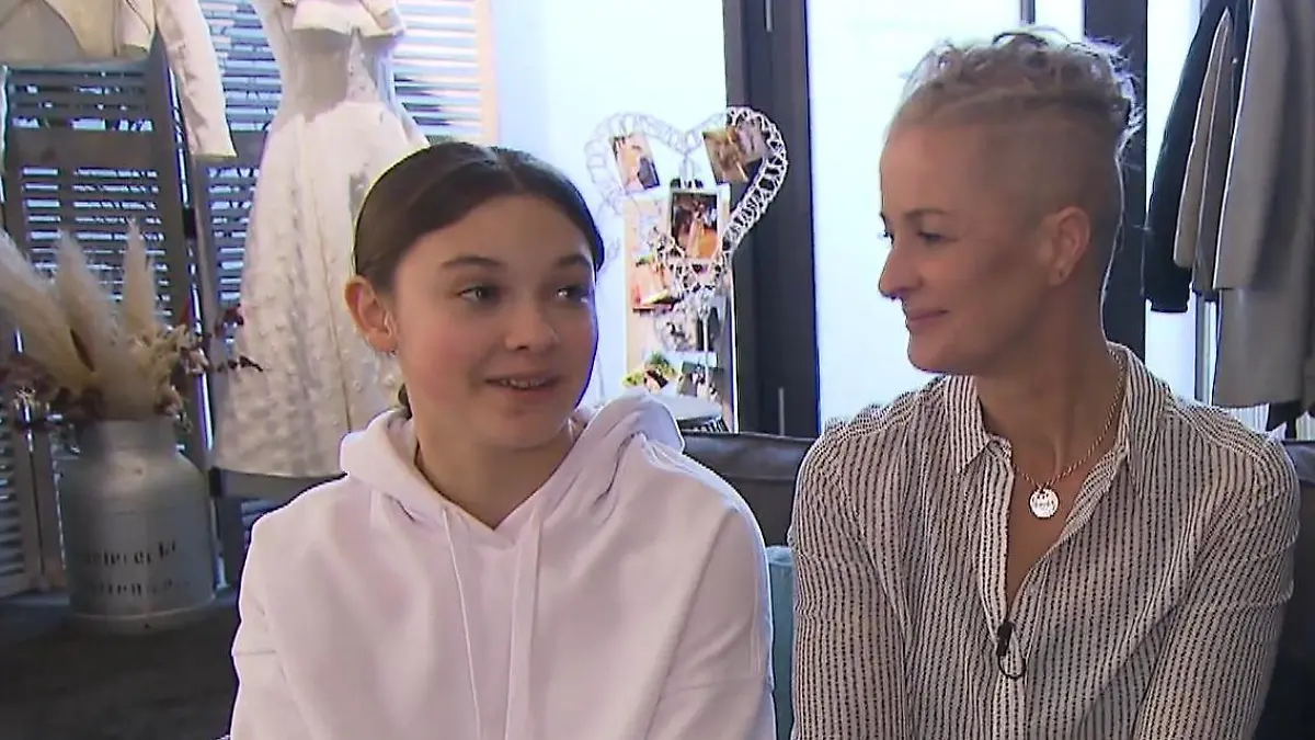 Zwischen Tüll und Tränen: Sportliche Frau mit rasierter Kurzhaarfrisur, daneben 14-jährige Mädchen mit langen braunen Haaren