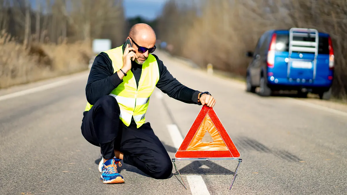 Mann setzt Warndreieck bei einem Unfall in ausreichender Entfernung vor sein Auto