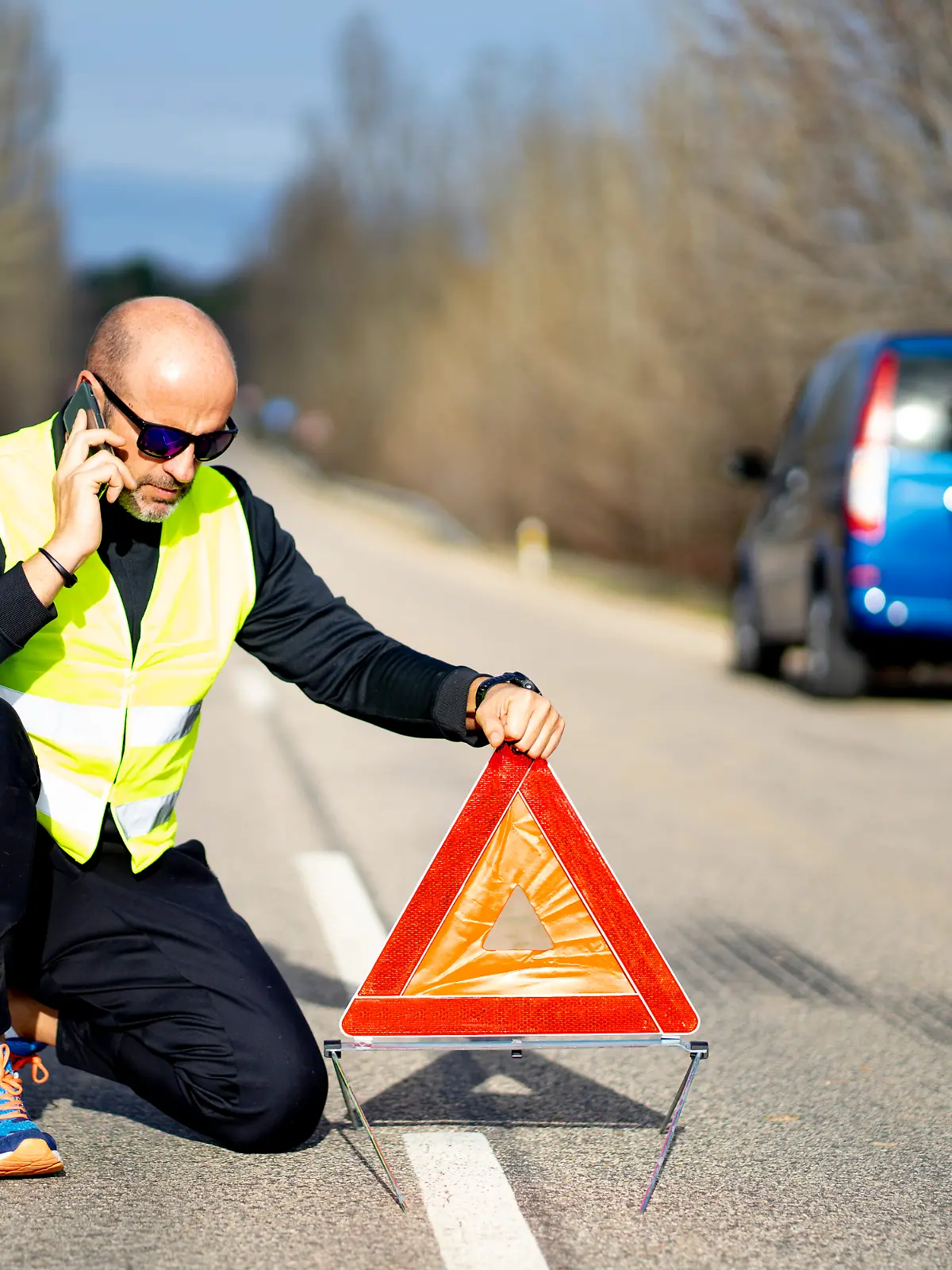 Mann setzt Warndreieck bei einem Unfall in ausreichender Entfernung vor sein Auto