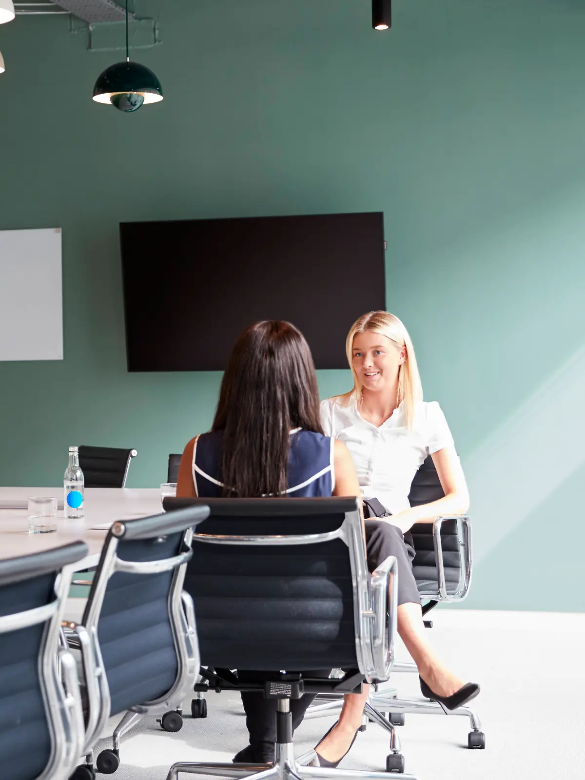 Bewerbungsgespräch unter vier Augen, zwei Frauen sitzen sich lächelnd gegebenüber in einem Büro mit einem langen Tisch und vielen Stühlen