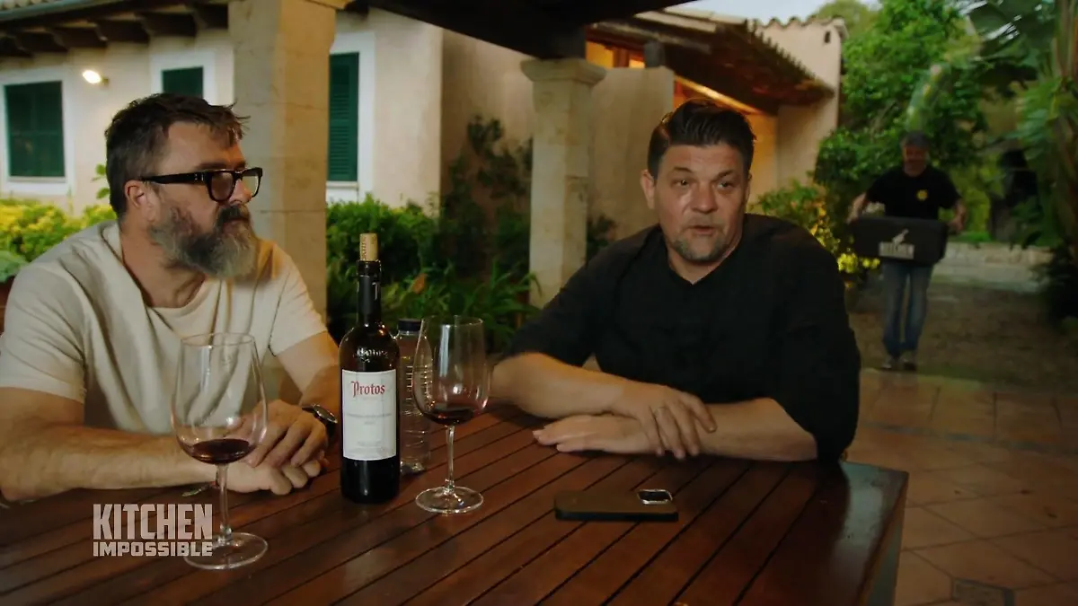 Tim Mälzer mit einem weiteren Mann an einem Tisch auf einer Terasse.