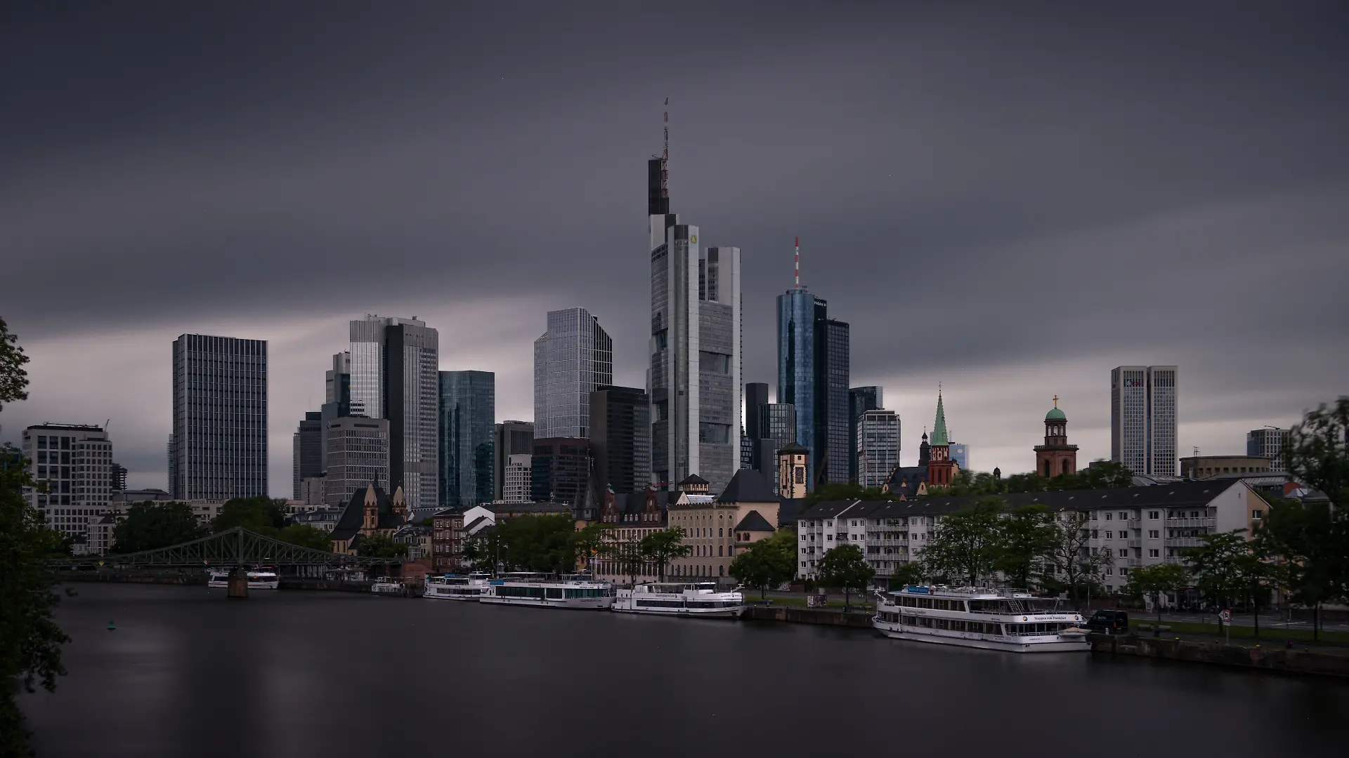 Tief dunkle Wolken ziehen am Morgen über die Frankfurter Skyline hinweg. Das Wetter zeigt sich in diesem Sommer wechselhaft. Auch in den kommenden Tagen sollen sich Wolken und Niederschläge mit Sonnenschein abwechseln, wobei die Temperaturen für Anfang Juli eher niedrig bleiben. (Langzeitbelichtung)