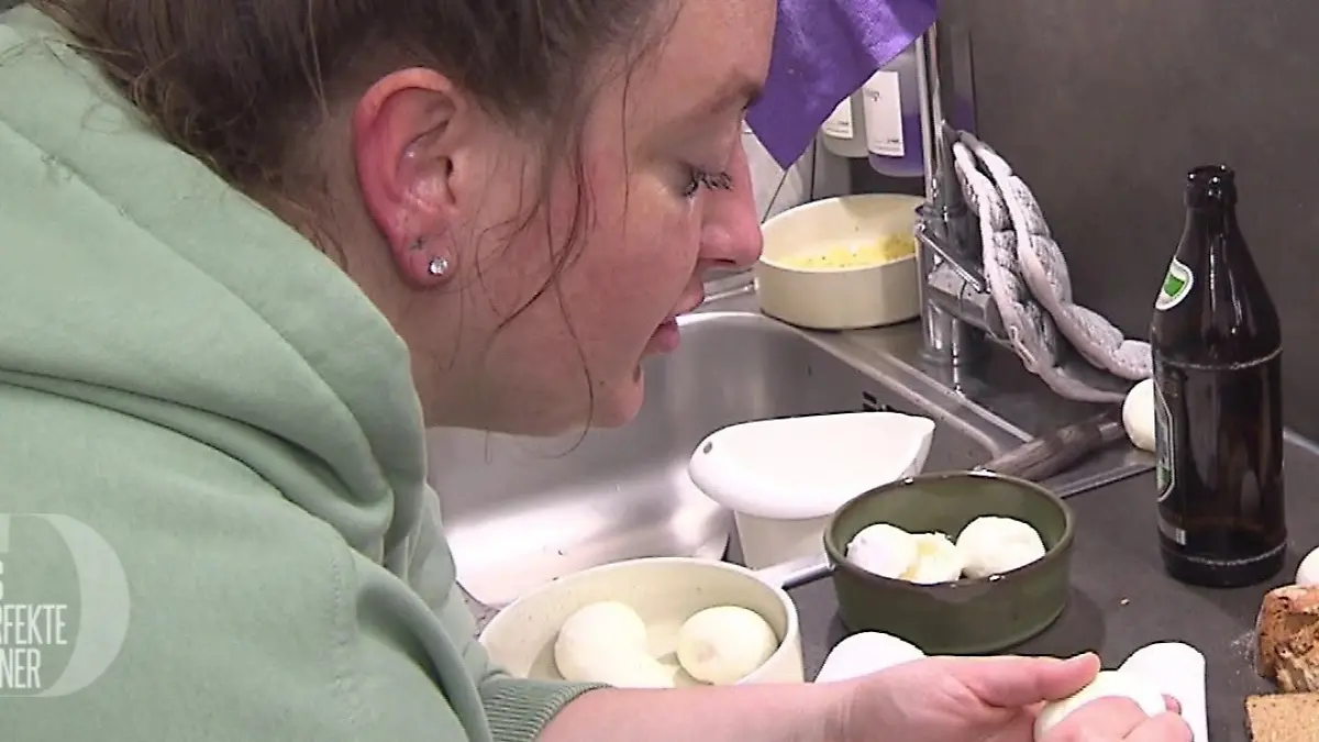 Sassi über ihre Küchenarbeitsplatte gebeugt, pellt ein Ei. 