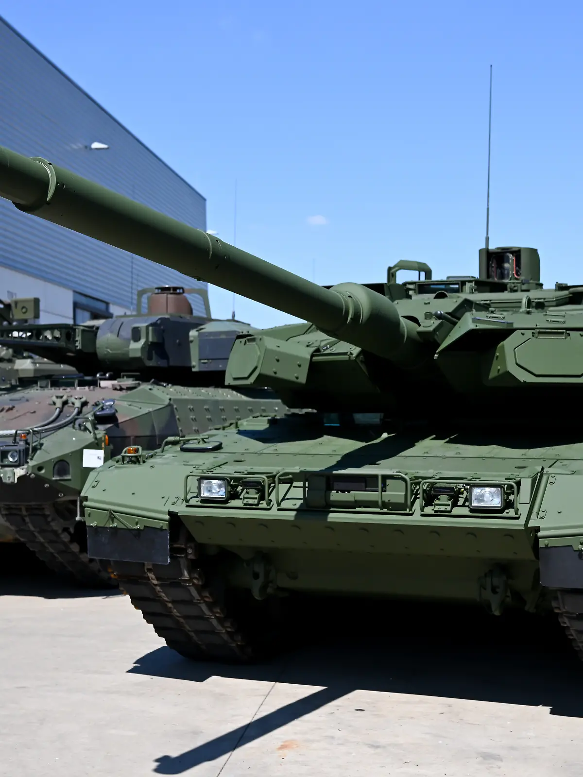 Ein Kampfpanzer Leopard 2 (r) steht auf dem Werksgelände des Unternehmens KNDS vor einer Werkshalle.