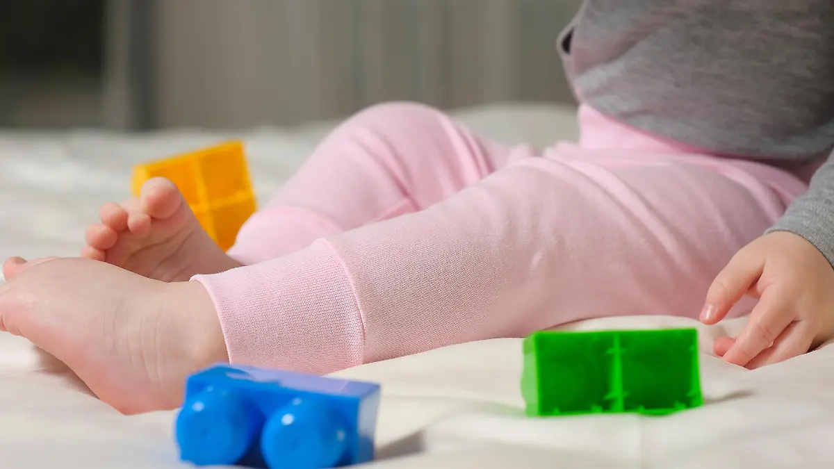 Cute cheerful child play with colorful toys at home. The legs of the child sitting on the bed