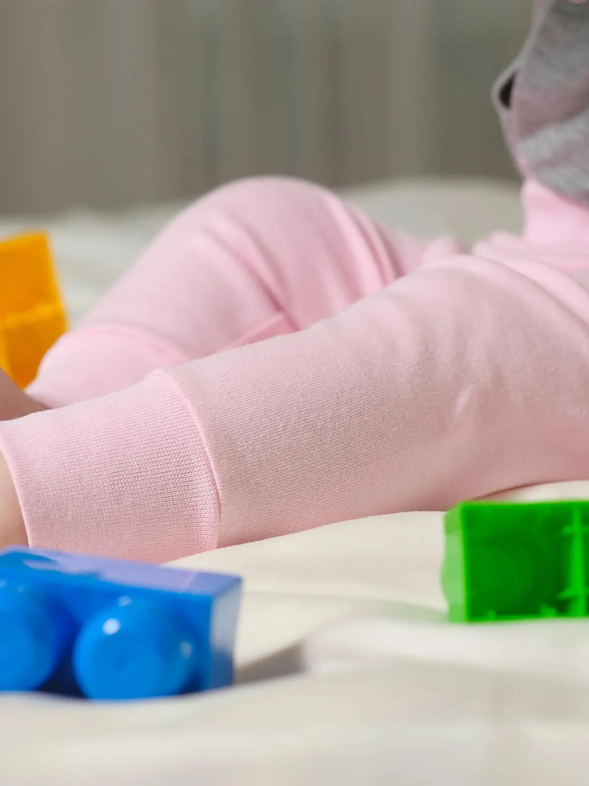 Cute cheerful child play with colorful toys at home. The legs of the child sitting on the bed