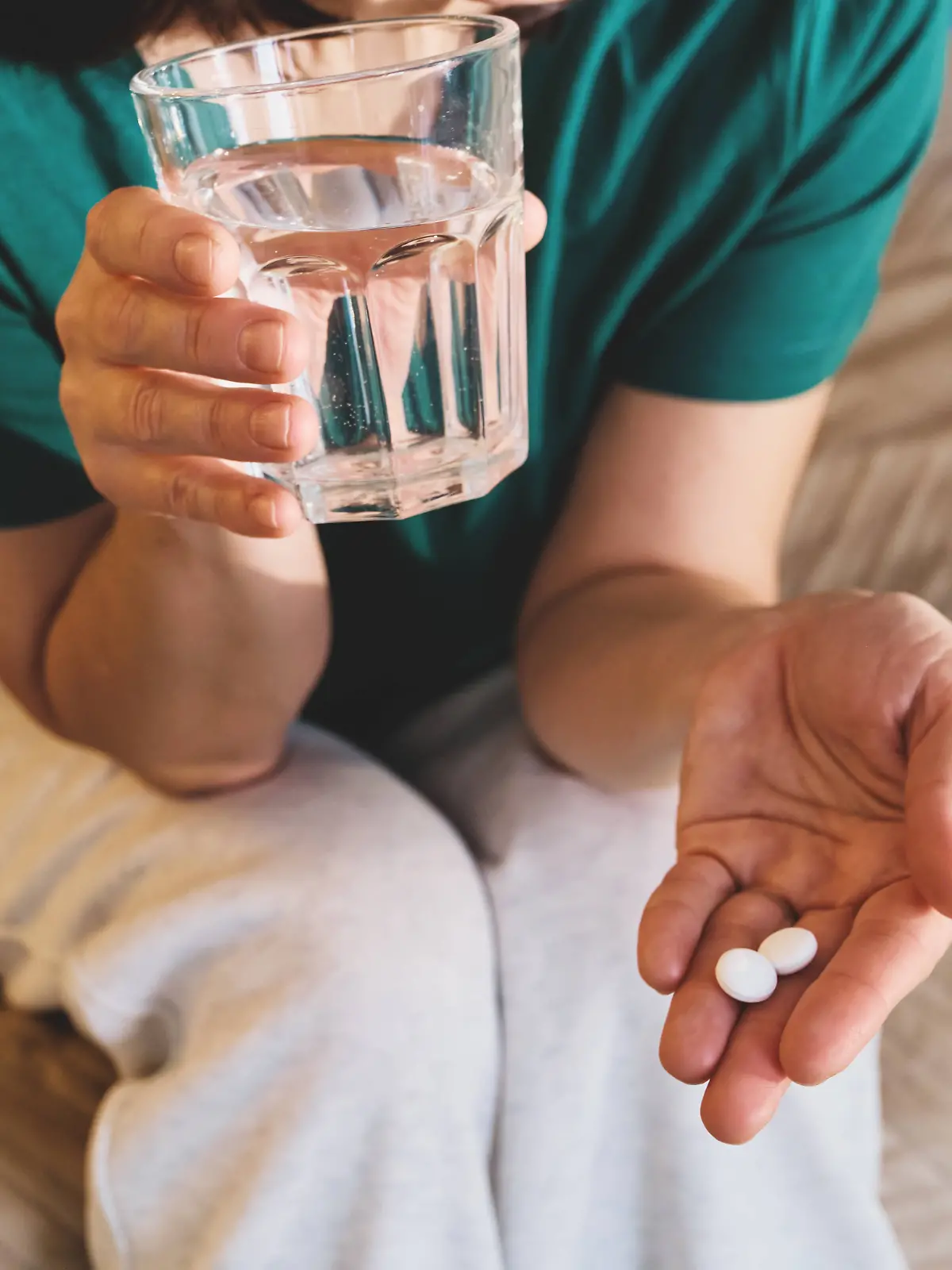 Frau, die Medikamente einnimmt, hält Tabletten und ein Glas Wasser 