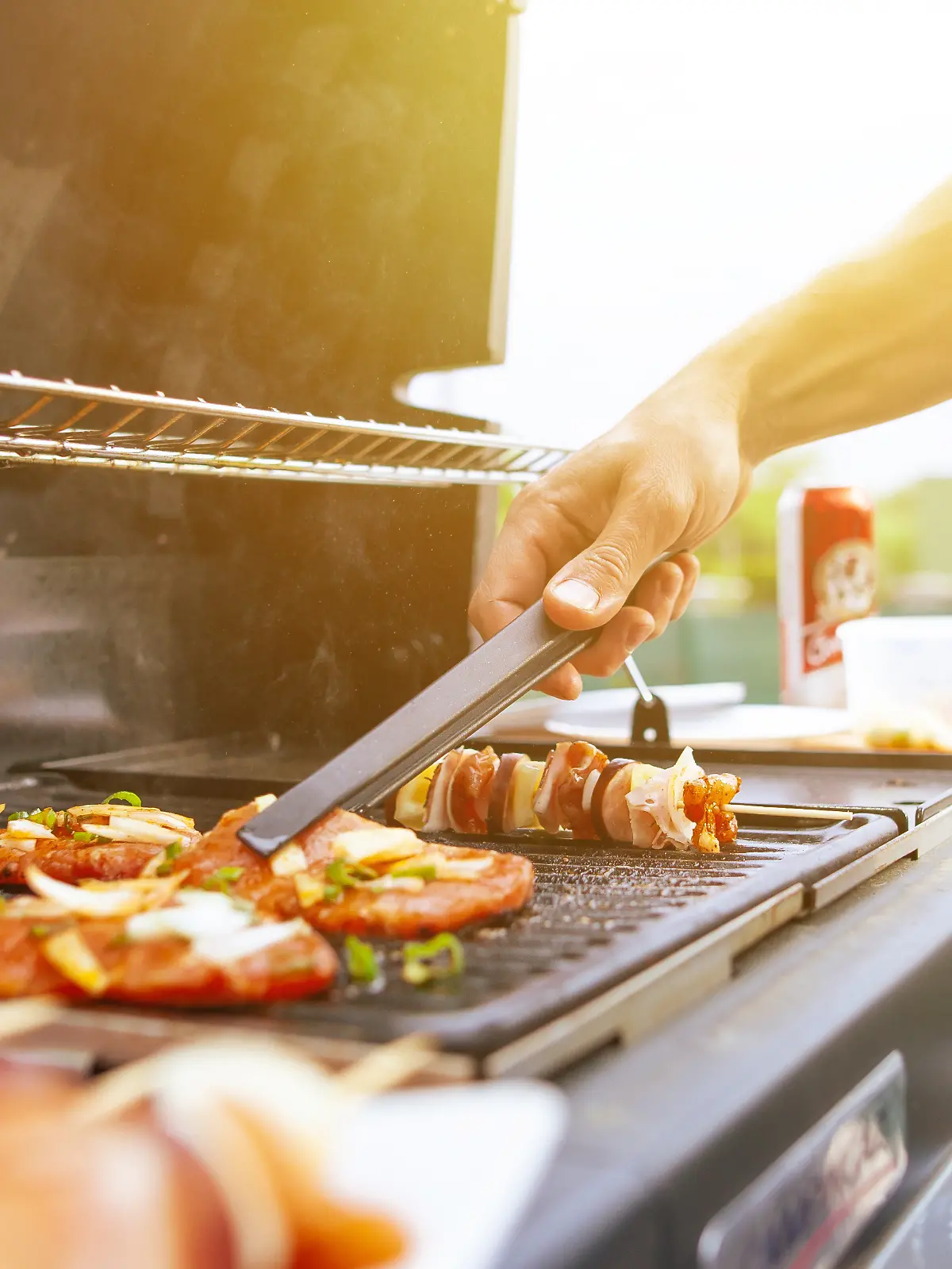 Junger Mann steht am Grill und wendet Fleisch