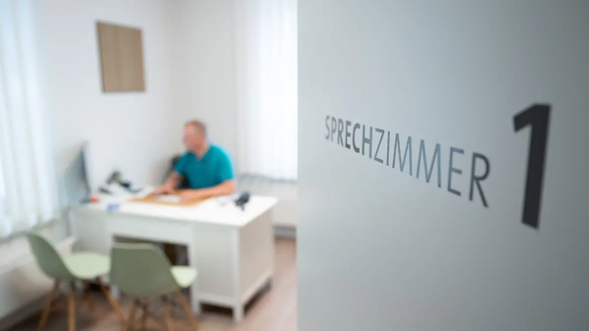 Ein Hausarzt sitzt in einem Sprechzimmer seiner Hausarztpraxis an einem Schreibtisch und arbeitet am Computer. Digitalisierung und der Einsatz von Software spielen eine zunehmende Rolle im Praxisalltag von Hausärzten.