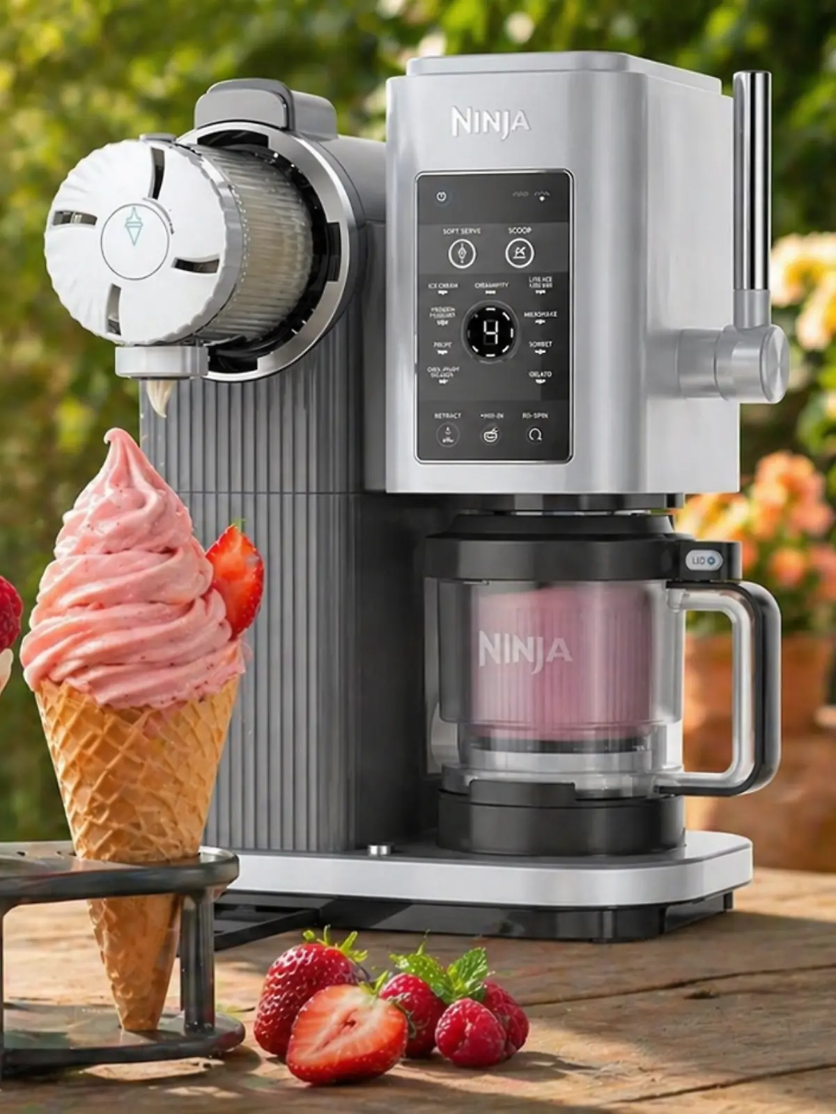 Eismaschine Ninja Creami mit drei Softeis in Waffeln, Früchten daneben auf einem Tisch und einem sommerlichen Garten im Hintergrund.