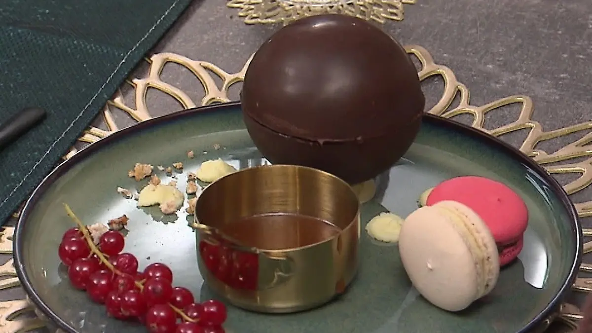Das perfekte Dinner: Tellerbild Dessert - eine gefüllte große Schokoladenkugel, Macarons, Sauce und Johannisbeeren