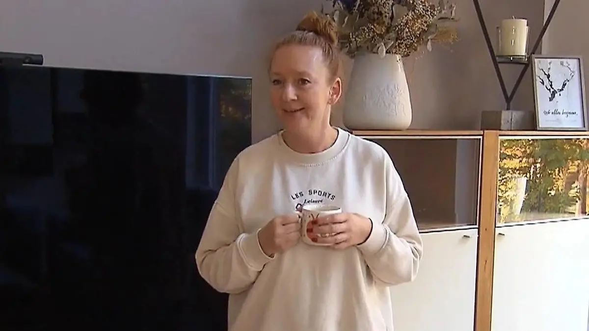 Anna steht mit einer Tasse in der Hand im Wohnzimmer.