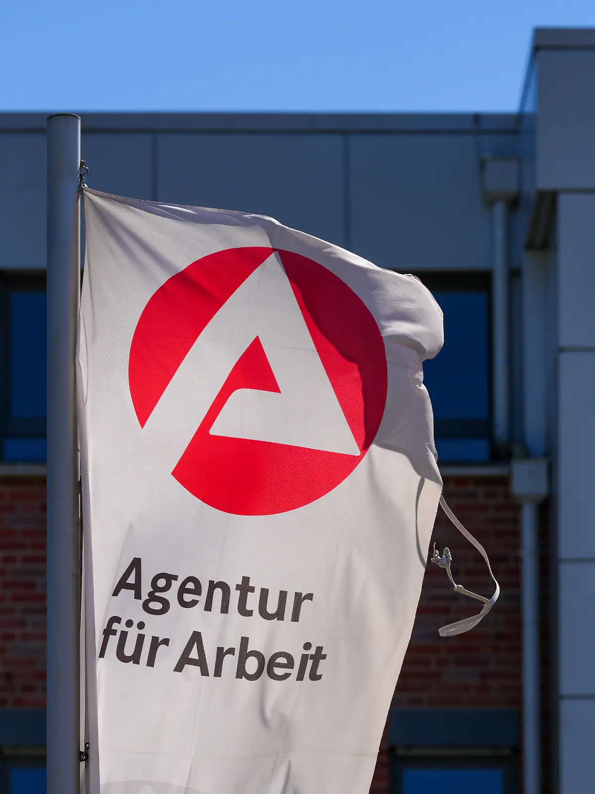 Eine Flagge mit dem Logo der Arbeitsagentur und dem Schriftzug «Agentur für Arbeit» weht an der Einfahrt in der Straße Horstweg.