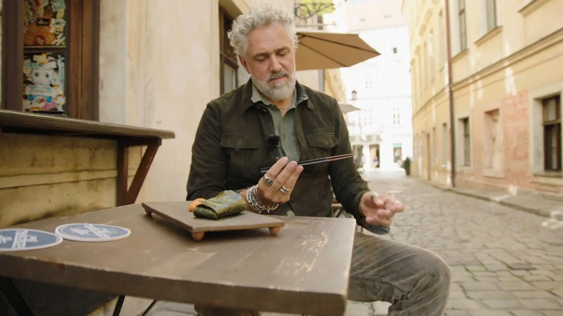 Roland schaut miesmutig auf Essstäbchen in seiner Hand, vor ihm eine Fischrolle.