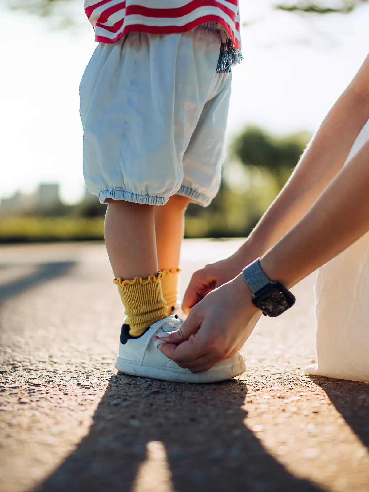 Ausschnitt einer fürsorglichen jungen Mutter, die ihrer kleinen Tochter im Park hilft und ihr beibringt, wie man Schnürsenkel bindet.