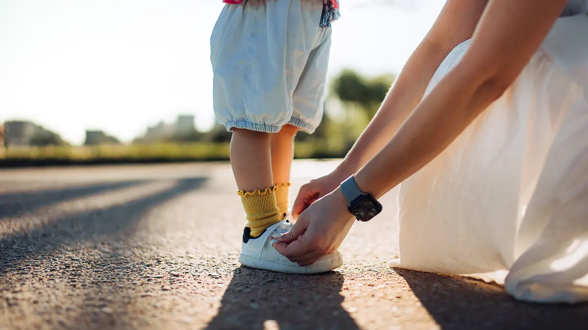 Ausschnitt einer fürsorglichen jungen Mutter, die ihrer kleinen Tochter im Park hilft und ihr beibringt, wie man Schnürsenkel bindet.