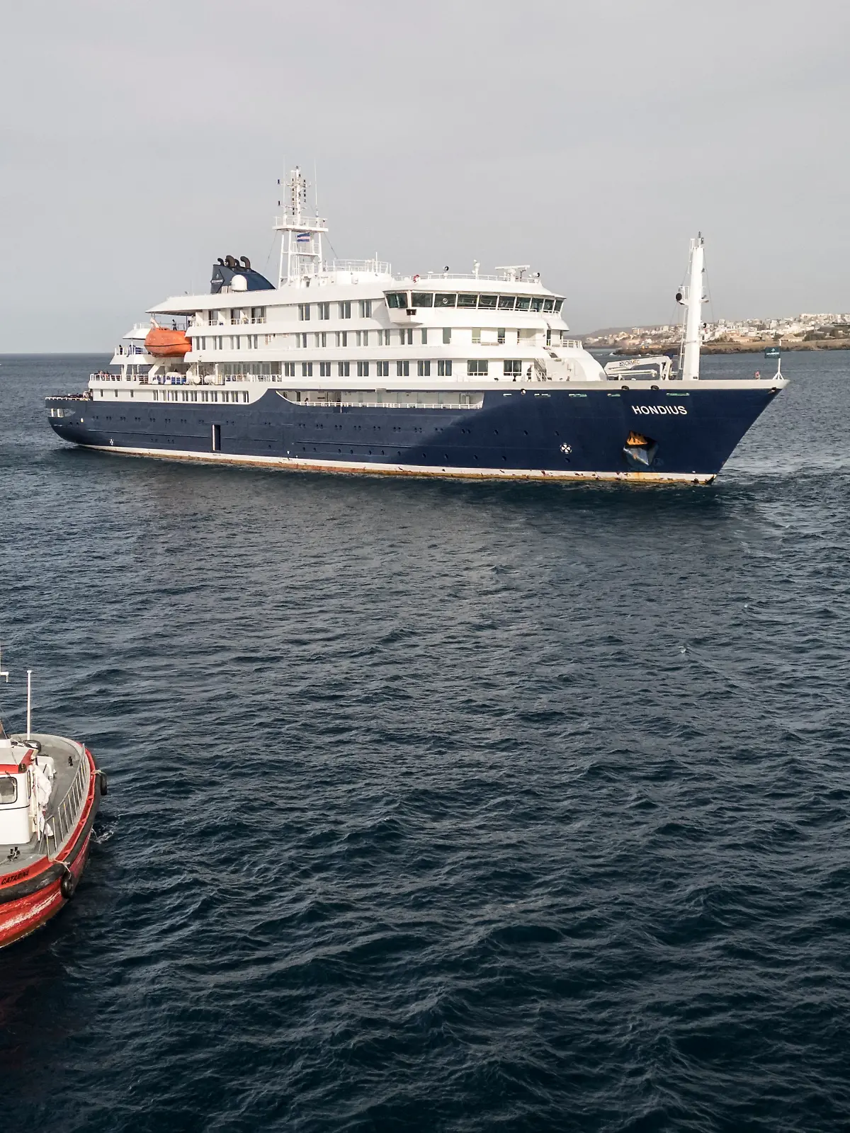 This aerial view shows a boat heading towards the port from the cruise ship MV Hondius, stationary off the port of Praia, the capital of Cape Verde, on May 6, 2026. Evacuations were taking place on May 6, 2026 from a cruise ship stricken with a deadly outbreak of hantavirus, the World Health Organization said, as experts confirmed a rare strain that can be transmitted between humans.
Three people, two crew members and one other person, thought to be infected with the virus were being taken off the MV Hondius, anchored off Cape Verde, the WHO said. (Photo by AFP)
