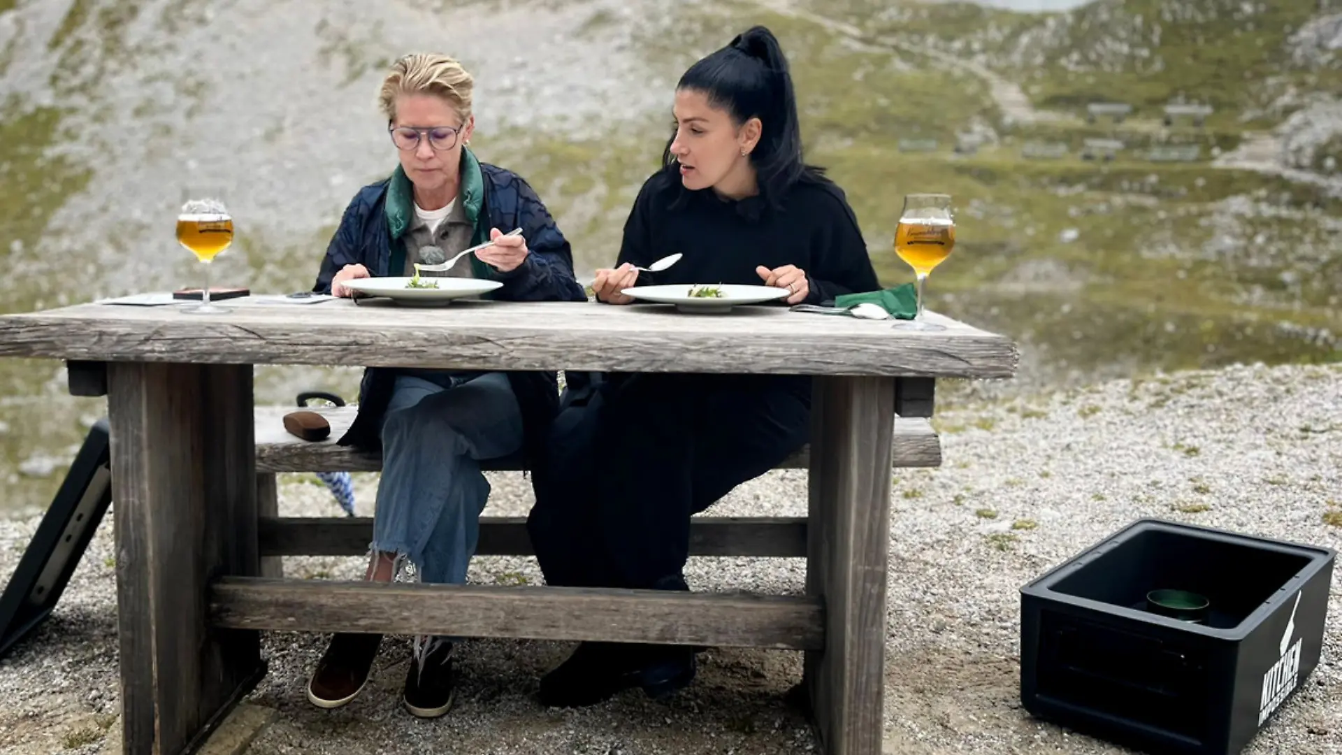 Die Köchinnen sitzen an einem Holztisch im freien und kosten ein Gericht.