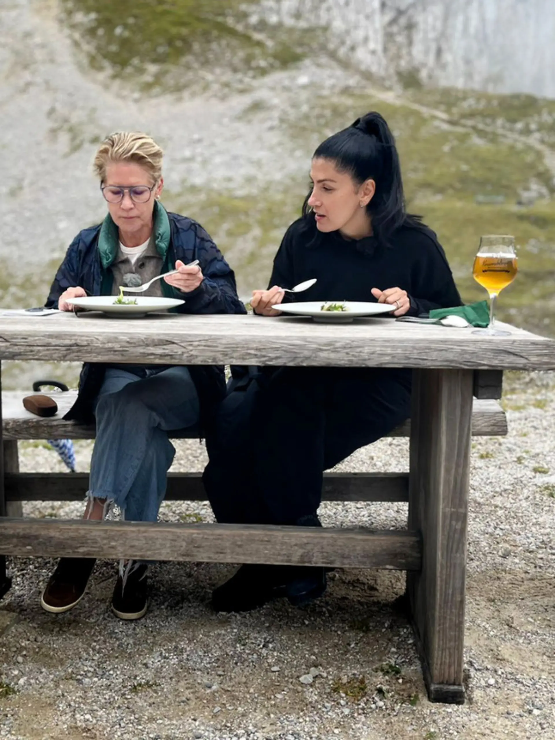 Die Köchinnen sitzen an einem Holztisch im freien und kosten ein Gericht.