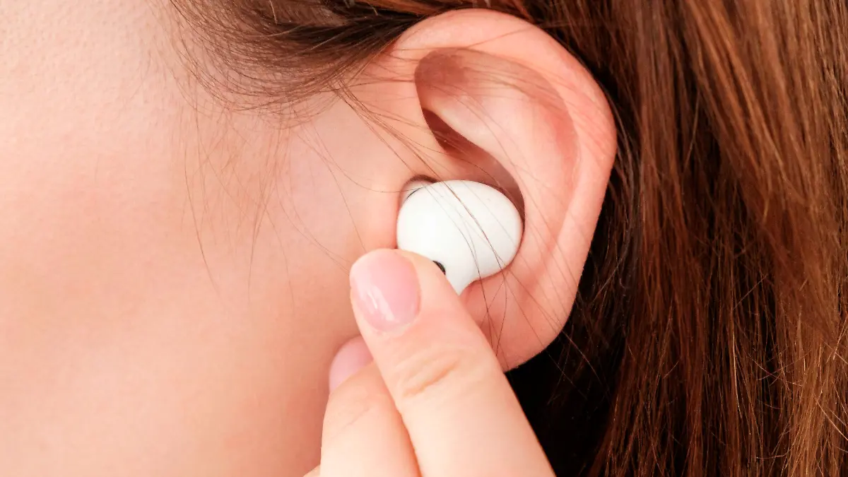 Woman inserts wireless headphone in the ear.