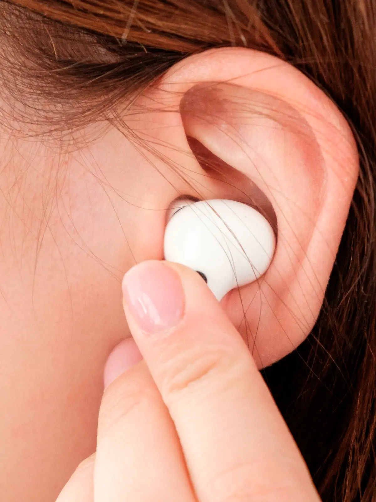 Woman inserts wireless headphone in the ear.