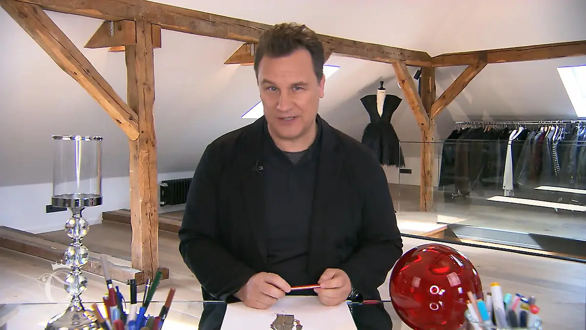 Shopping Queen: Guido Maria Kretschmer sitzt am Schreibtisch und verkündet das Wochenmotto in die Kamera
