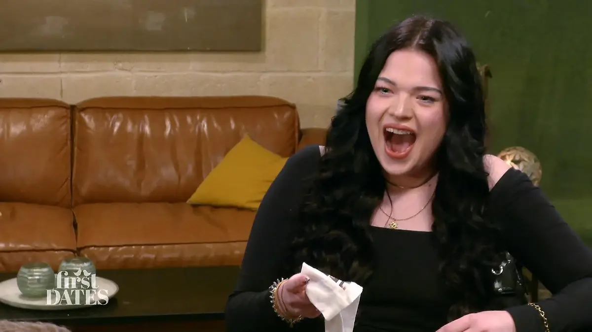 First Dates – Ein Tisch für zwei: Junge Frau mit langen schwarzen Haaren und schwarzem Outfit hält lachend eine weiße Socke in der Hand