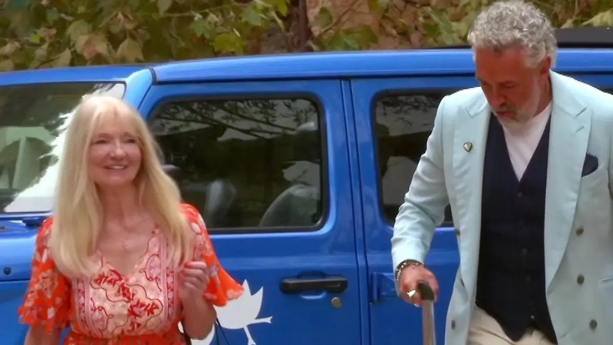 Vera steigt aus einem Auto, Roland Trettl schiebt neben ihr einen Rollkoffer.