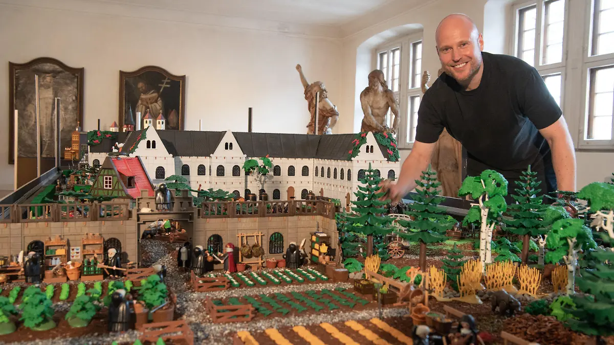 14.07.2021, Hessen, Eltville: Der Künstler Oliver Schaffer steht im Kloster Eberbach im Rheingau an einem Modell des Klosters, welches er in wochenlanger Kleinarbeit aus mehr als 50.000 Einzelteilen zu einem Diorama zusammengesetzt hat. Zu dem Kloster im Maßstab 1:23 gehören auch mehr als 5000 Figuren wie Menschen und Tiere. (zu dpa: «Playmobil-Ausstellung öffnet in Kloster Eberbach») Foto: Boris Roessler/dpa - ACHTUNG: Nur zur redaktionellen Verwendung im Zusammenhang mit der aktuellen Berichterstattung über die Ausstellung. +++ dpa-Bildfunk +++