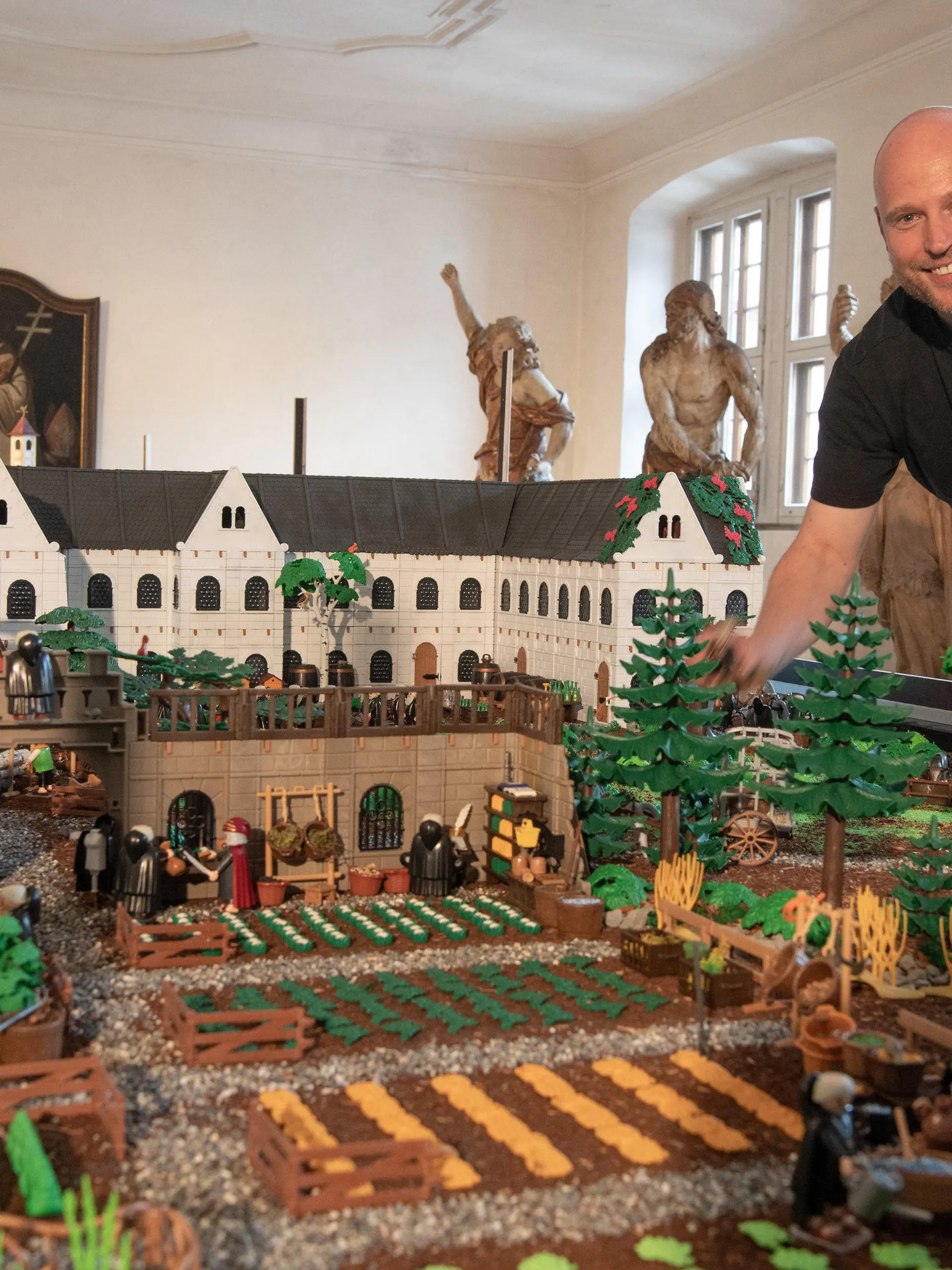 14.07.2021, Hessen, Eltville: Der Künstler Oliver Schaffer steht im Kloster Eberbach im Rheingau an einem Modell des Klosters, welches er in wochenlanger Kleinarbeit aus mehr als 50.000 Einzelteilen zu einem Diorama zusammengesetzt hat. Zu dem Kloster im Maßstab 1:23 gehören auch mehr als 5000 Figuren wie Menschen und Tiere. (zu dpa: «Playmobil-Ausstellung öffnet in Kloster Eberbach») Foto: Boris Roessler/dpa - ACHTUNG: Nur zur redaktionellen Verwendung im Zusammenhang mit der aktuellen Berichterstattung über die Ausstellung. +++ dpa-Bildfunk +++