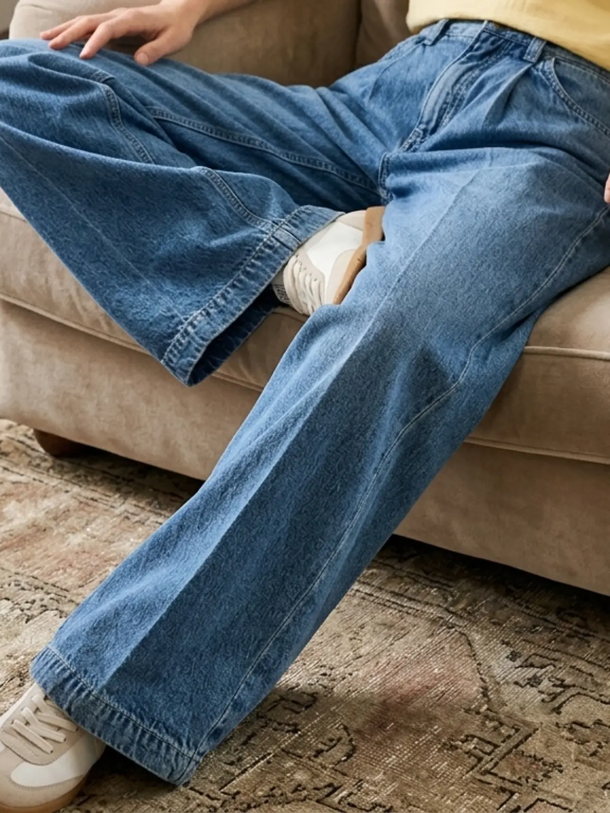 Eine Frau trägt eine Jeans von Bonprix und sitzt entspannt auf einem Sessel im Wohnzimmer.