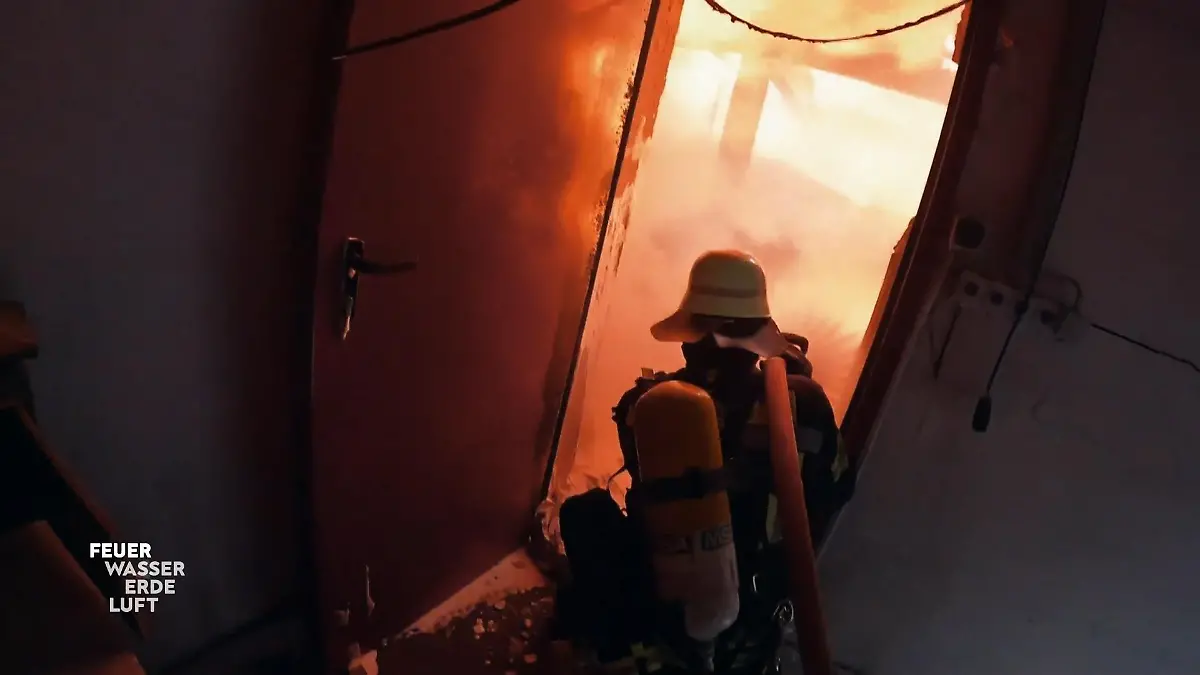 Feuer, Wasser, Erde, Luft: Feuerwehrmann in voller Montur bekämpft einen Brand in einer dunklen Lagerhalle